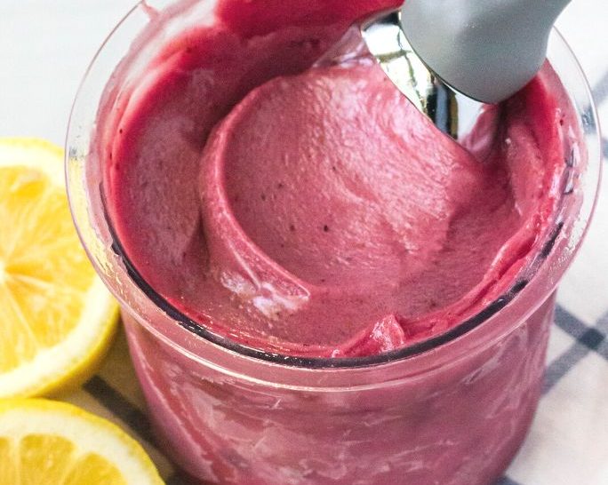 ninja creami berry lemonade sorbet in a pint container with an ice cream scoop in it.