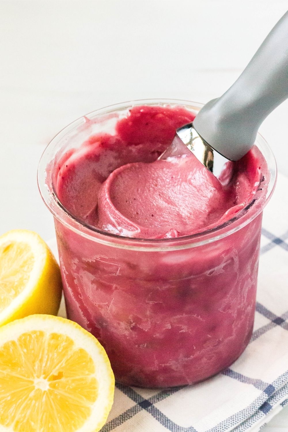 a Ninja Creami pint filled with berry lemon sorbet. An ice cream scoop is in the pint, and pieces of fresh lemons are next to the pint