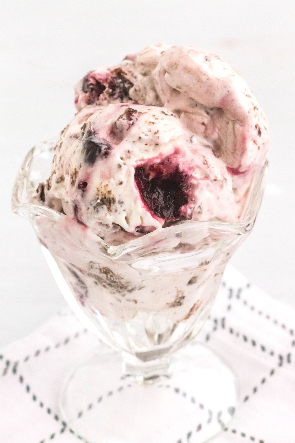 a glass ice cream dish serves scoops of homemade black forest ice cream, showing the chocolate pieces and sweet dark cherries.