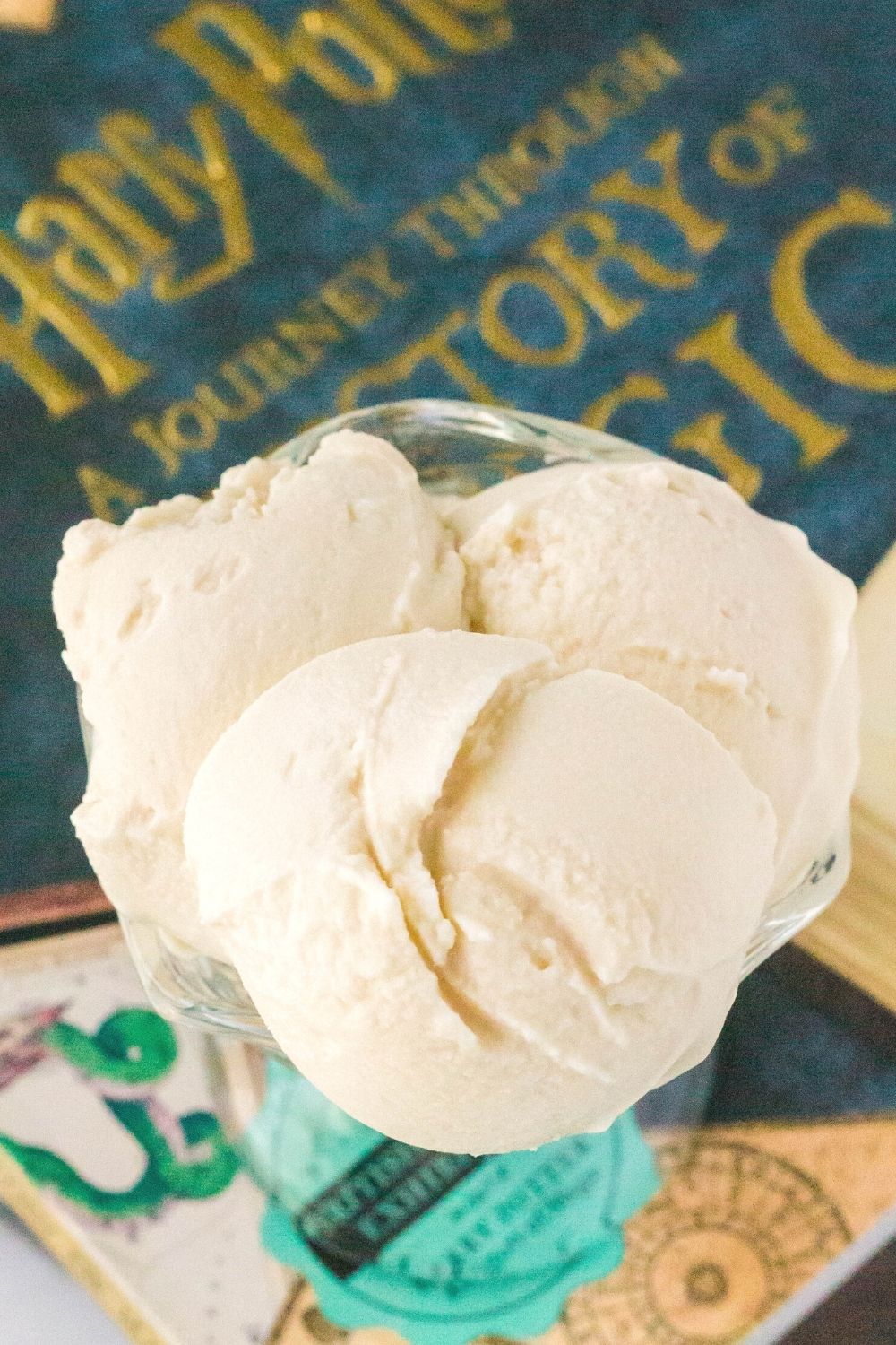 three scoops of Ninja Creami butterbeer ice cream served in a glass dessert cup next to a Harry Potter book