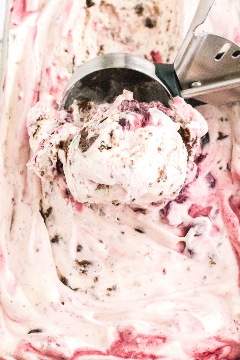 close-up view of a loaf pan of black cherry ice cream with an ice cream scoop in it