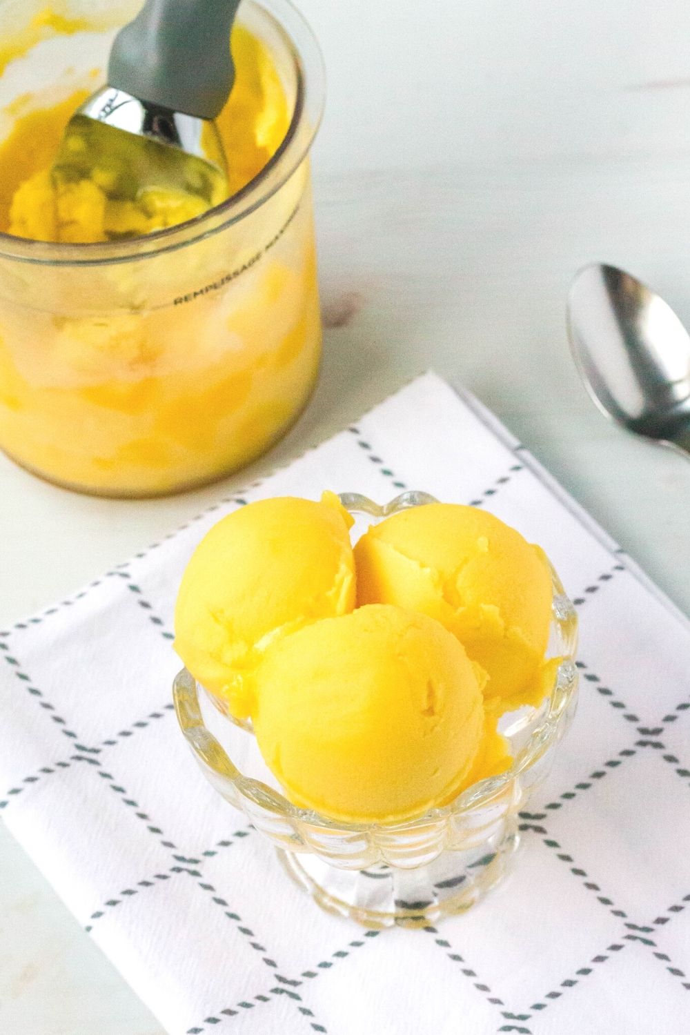 three scoops of mango sorbet made in the ninja creami are served in a glass dish. A pint container is in the background.