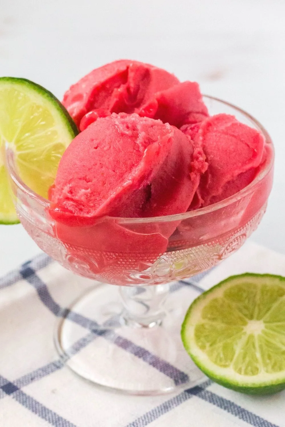 a glass dish serves three scoops of Ninja Creami cherry lime sorbet. The glass is garnished with a lime slice.