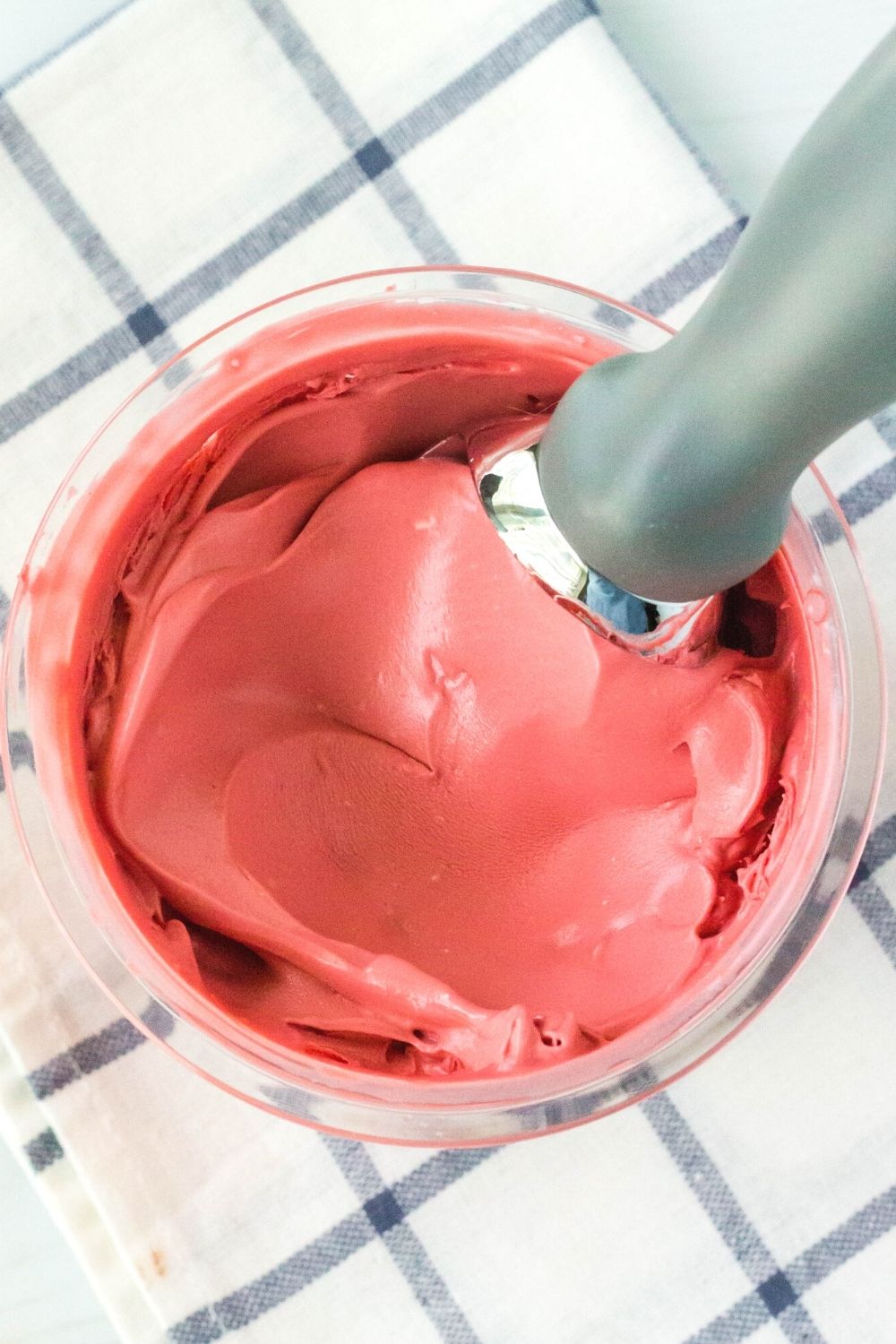 overhead view of the top surface of a pint of ninja creami red velvet ice cream with an ice cream scoop in it.