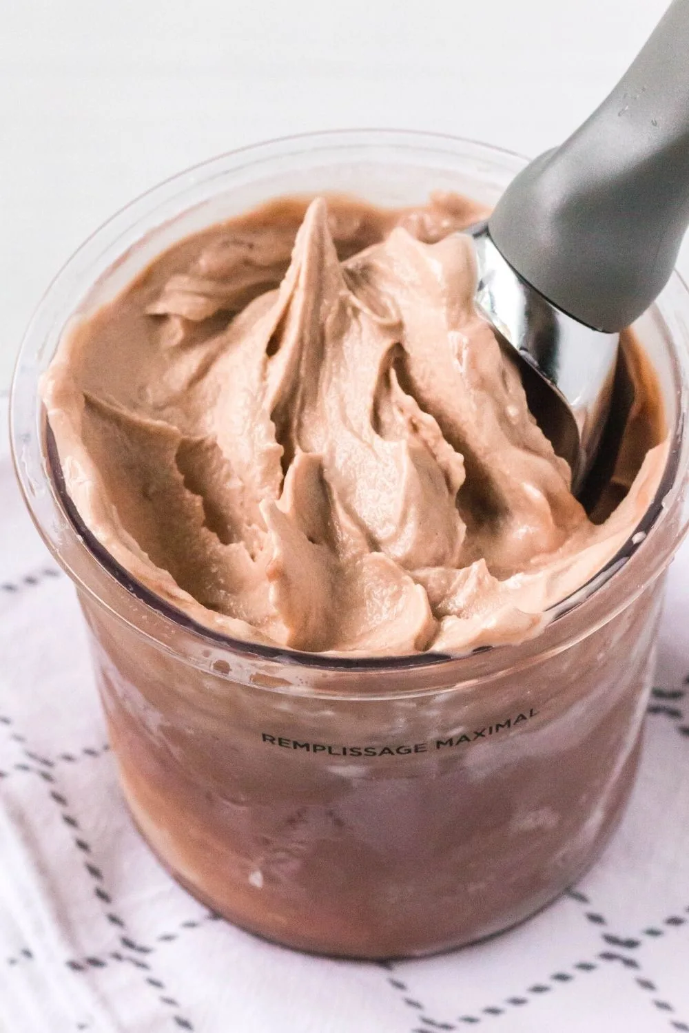 chocolate protein ice cream in a Ninja Creami pint, with an ice cream scoop in the ice cream.