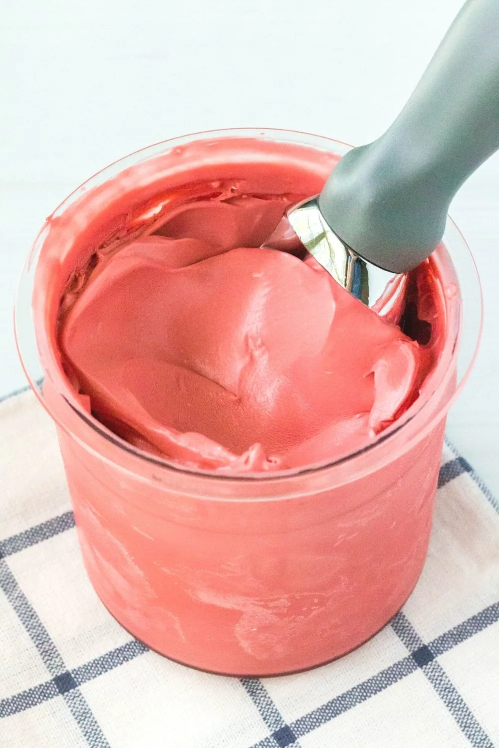 close-up view of a Ninja Creami pint filled with red velvet cake batter ice cream. An ice cream scoop is swirling the top of the ice cream.