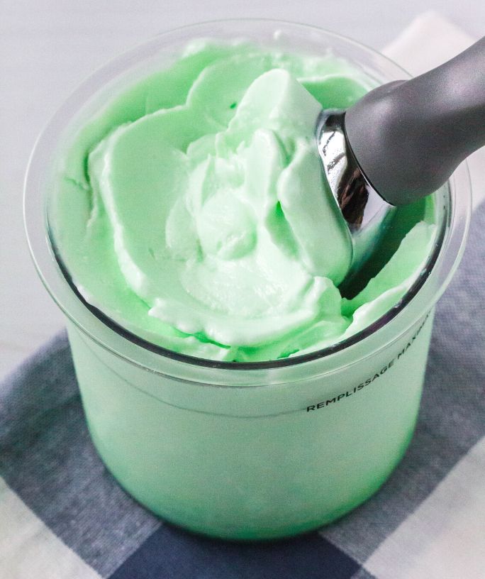 Ninja Creami lime sherbet in a pint container, with an ice cream scoop in the sherbet.