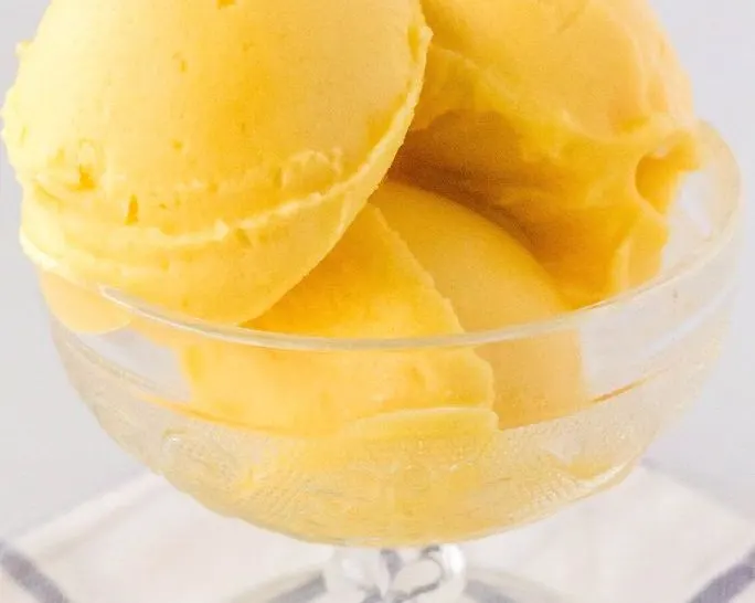 three scoops of Ninja Creami peach sorbet served in a glass dessert cup.