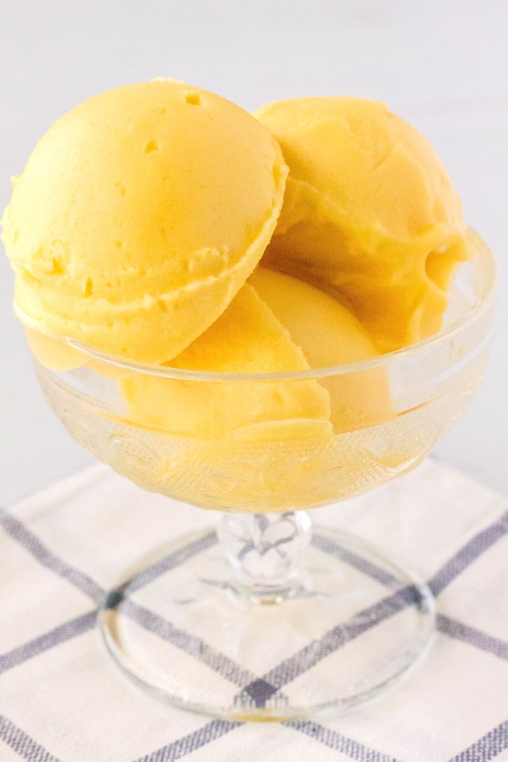 side view of a glass dessert cup filled with three scoops of peach sorbet made in the Ninja Creami machine.