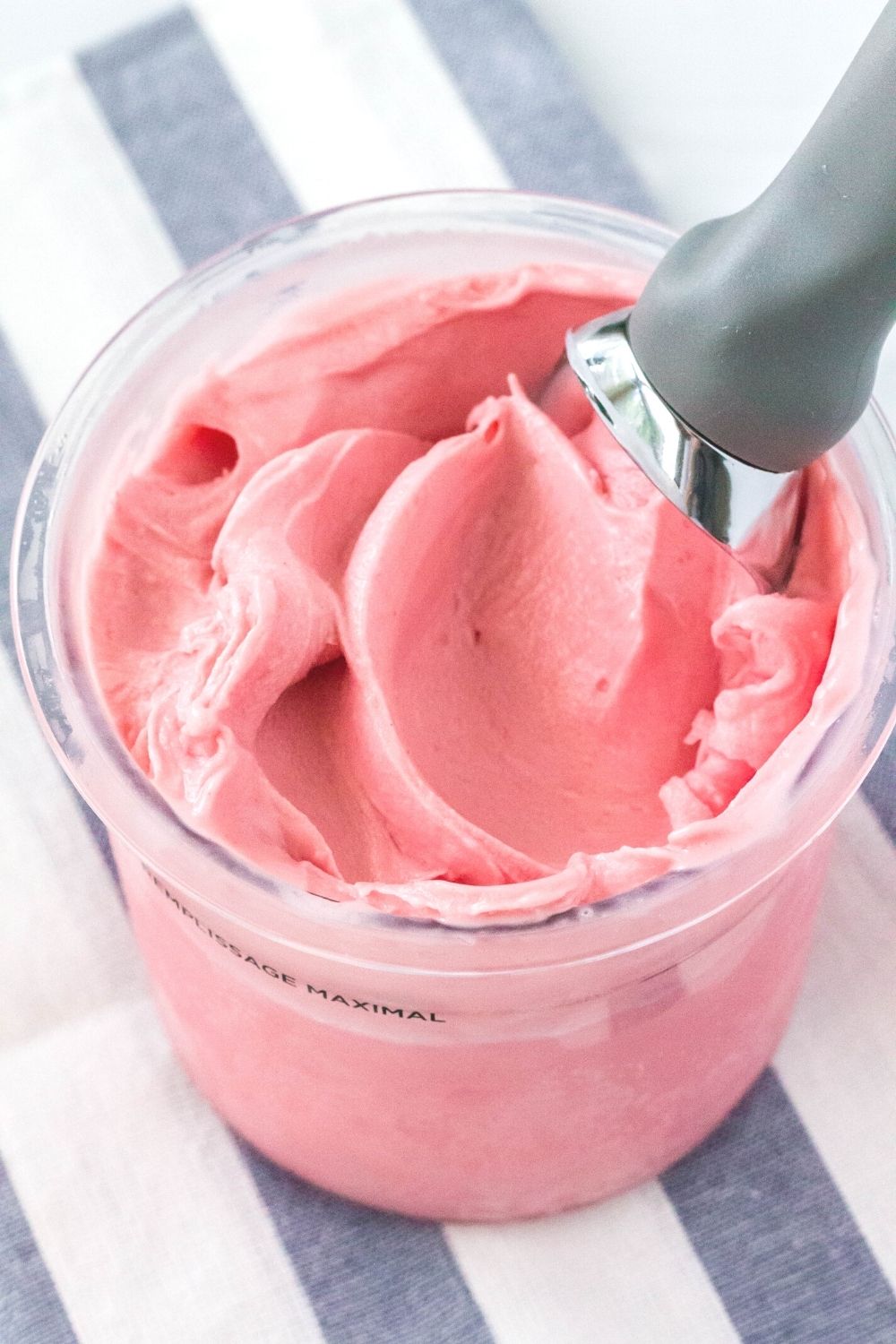 a Ninja Creami pint container filled with pink cherry cheesecake ice cream. An ice cream scoop is in the pint.