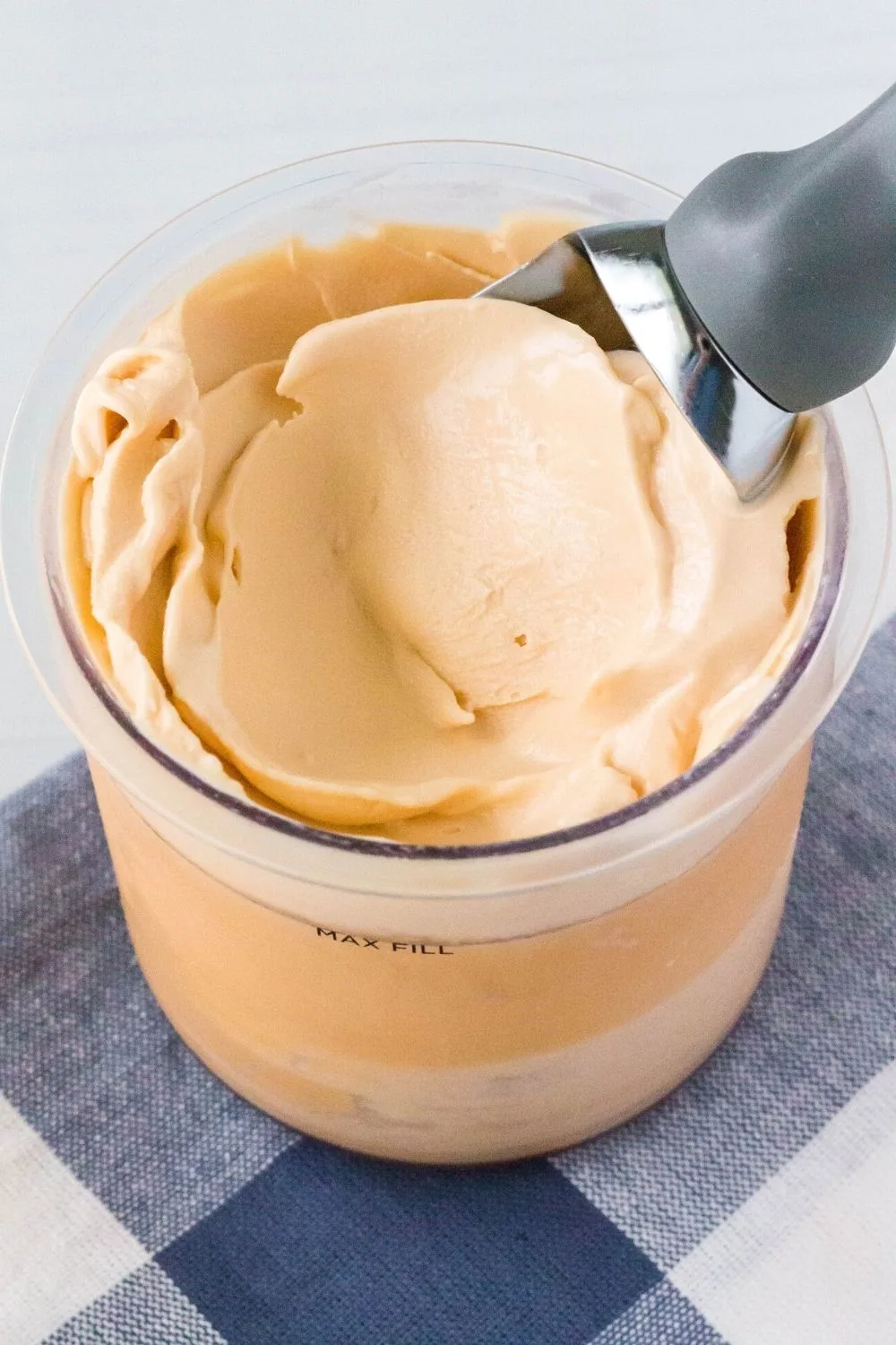 a Ninja Creami pint container filled with butterscotch ice cream. An ice cream scoop is in the pint.