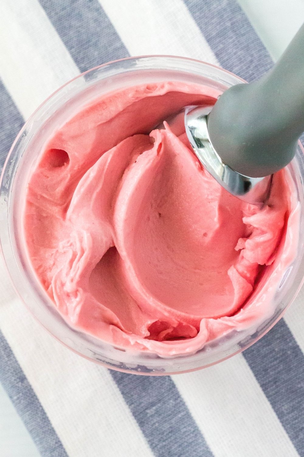overhead view of a pint container filled with ninja creami cherry cheesecake flavored ice cream, with a scoop in the ice cream giving the top a swirled appearance.