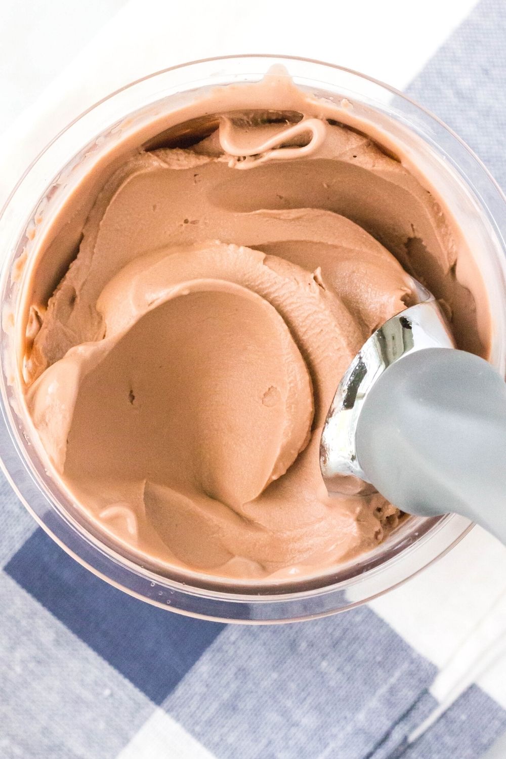 overhead view of the top of a Ninja Creami pint filled with chocolate pudding ice cream. An ice cream scoop swirls the top of the ice cream, showing its creamy, silky texture.