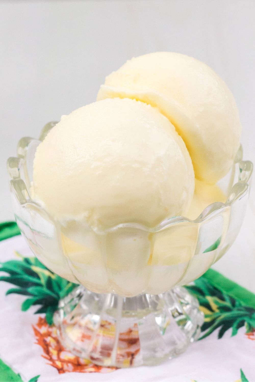 close-up side view of two scoops of Ninja Creami pineapple coconut ice cream in a glass dish.