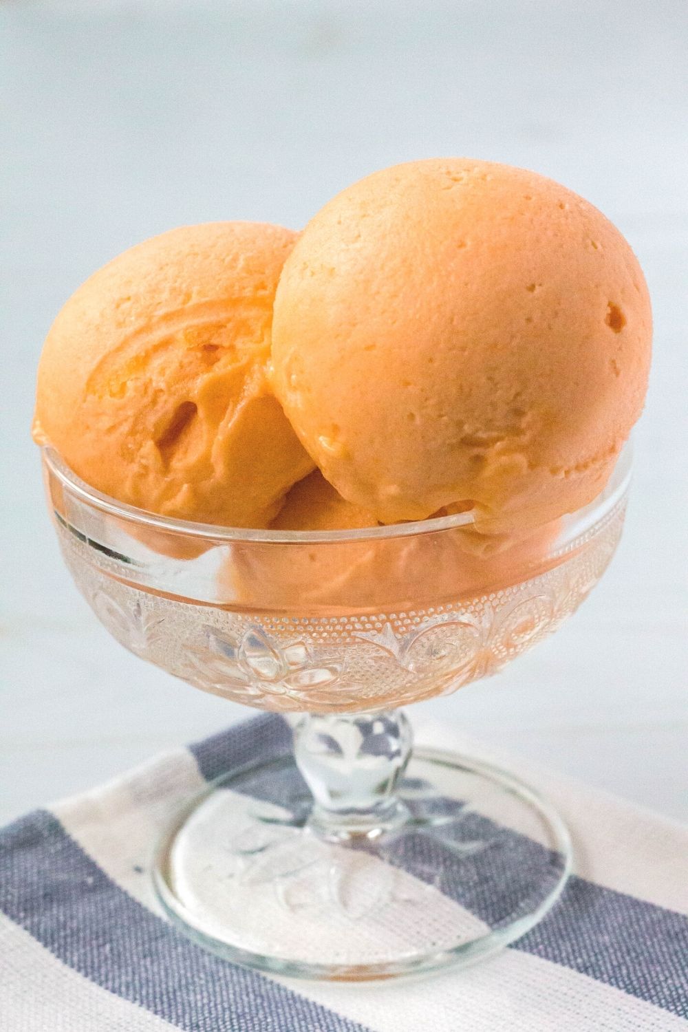 close-up side view of a glass dessert cup with scoops of orange sorbet made from Jell-O in it.