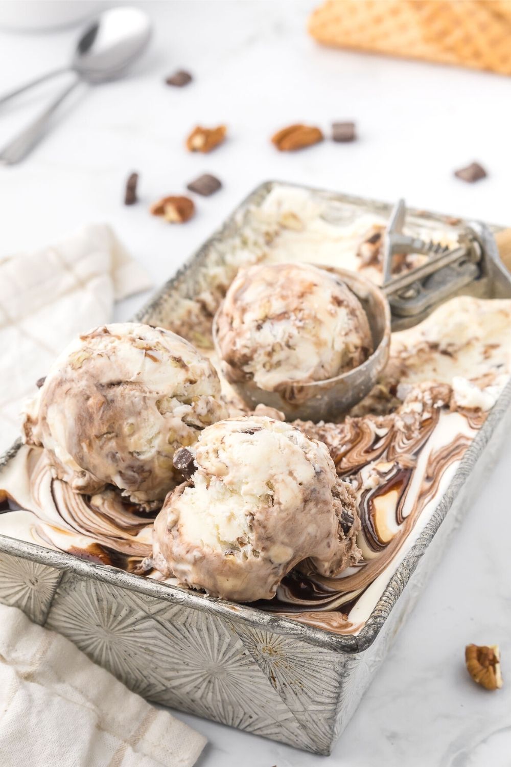 an ice cream scoop is scooping rounds of homemade turtle ice cream from a loaf pan.