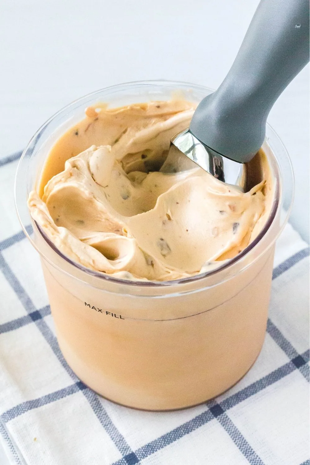 a Ninja Creami pint container filled with Butterfinger flavored ice cream. An ice cream scoop is in the pint.