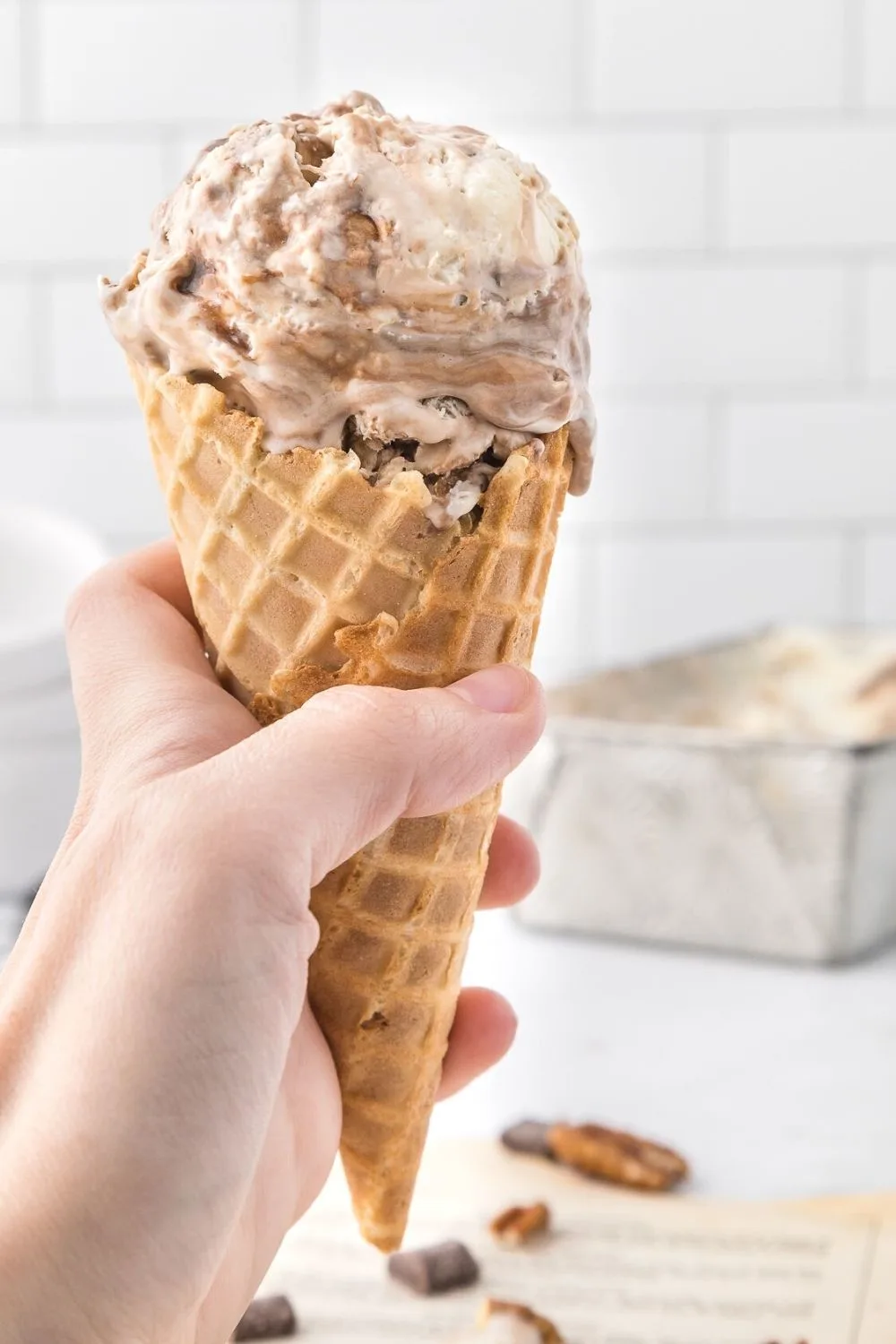 a woman's hand holds a waffle cone with a hearty scoop of turtle ice cream in it.
