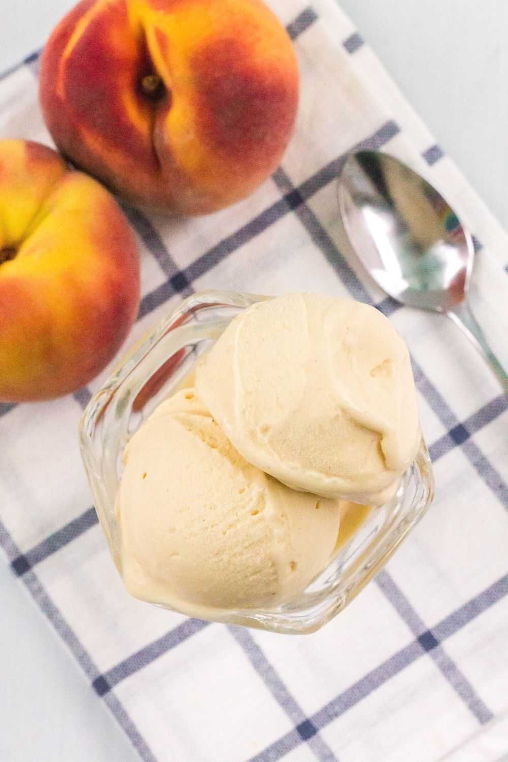 overhead view of two scoops of ninja creami peach ice cream in a glass dish, with two fresh peaches next to it
