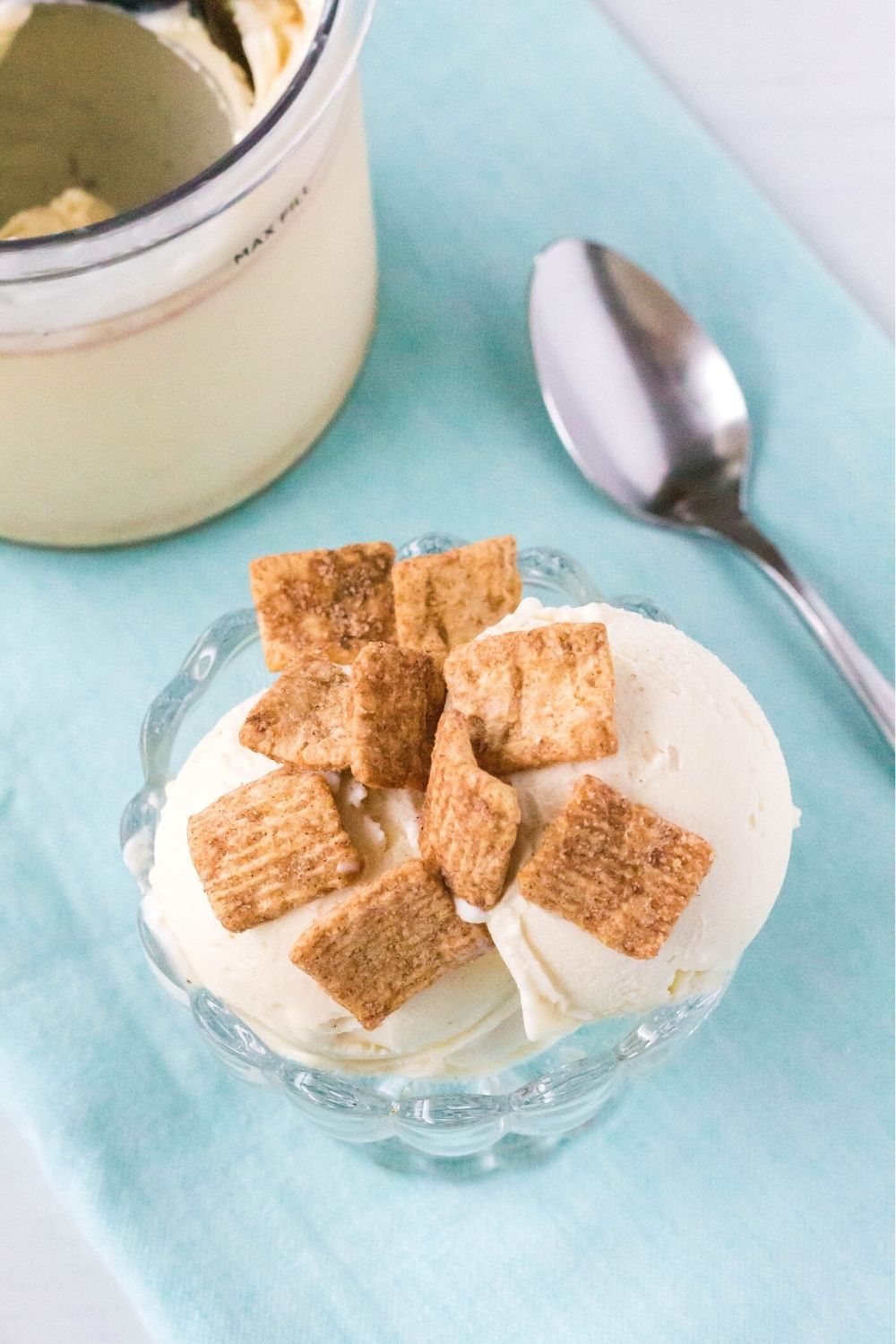 a glass dish serves Ninja Creami Cinnamon Toast Crunch Cereal ice cream. The pint container and a spoon are in the background.
