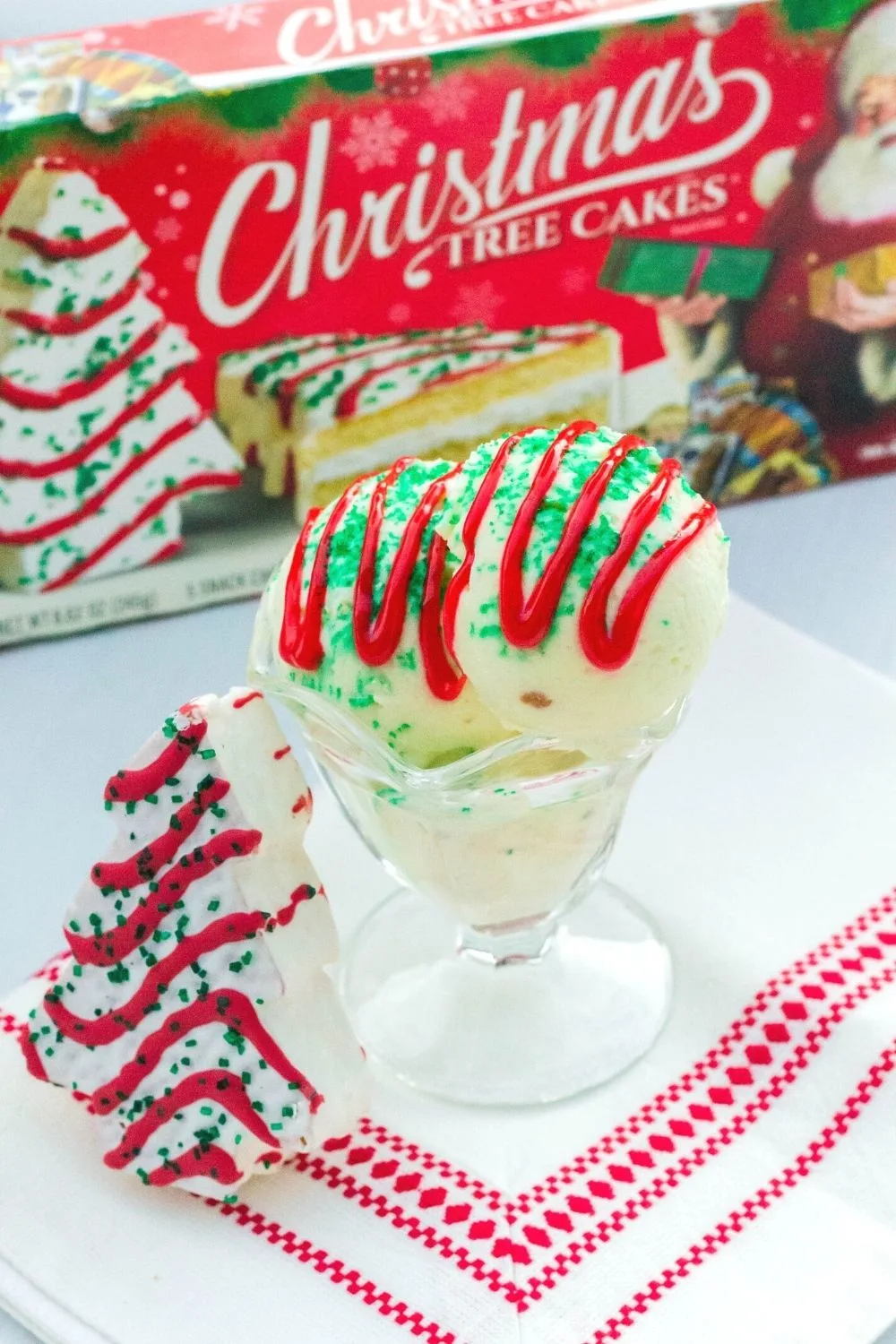 a glass dish of Christmas Tree Cake ice cream, with a Little Debbie snack cake next to it, and a box of Christmas Tree Cakes in the background.