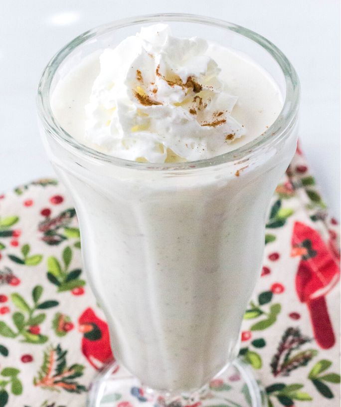 ninja creami eggnog milkshake served in a tall glass, topped with whipped cream and a sprinkle of cinnamon