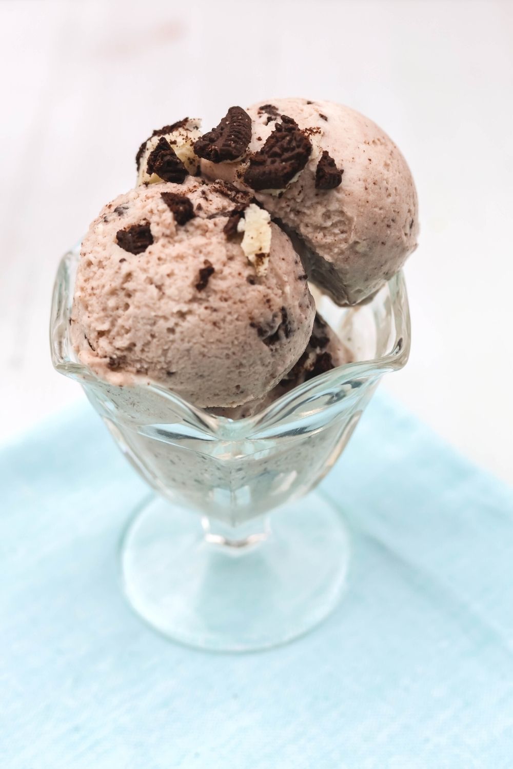 close-up view of scoops of Ninja Creami high protein cookies and cream ice cream served in a glass ice cream dish. Oreo cookie pieces are sprinkled over the scoops.