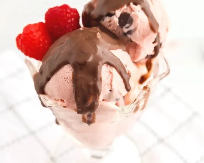 Ninja Creami raspberry chocolate chip ice cream served in a glass dish, topped with chocolate shell topping and garnished with raspberries.