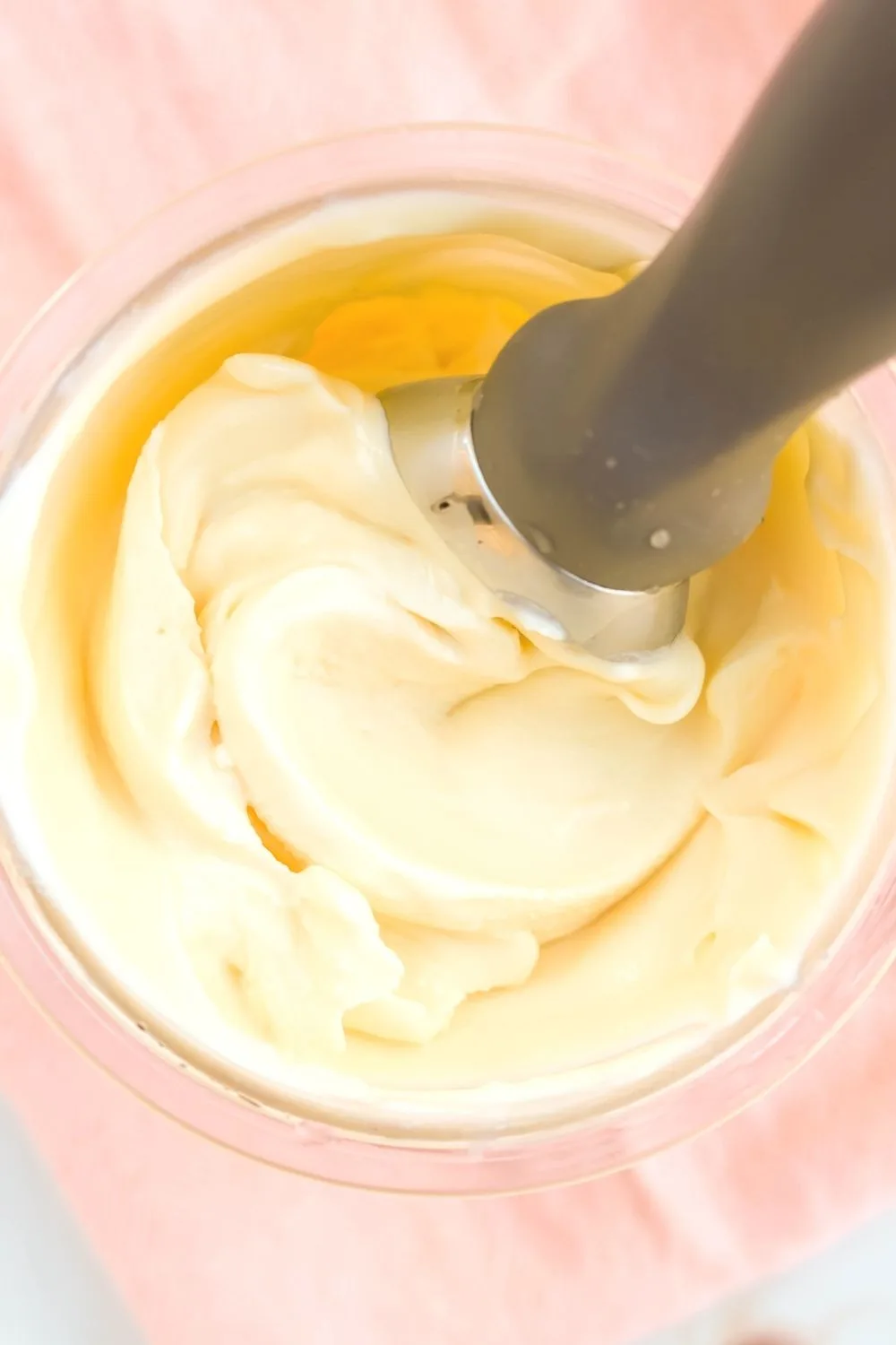 overhead close-up view of vanilla sweet cream ice cream in a Ninja Creami pint container, with an ice cream scoop in the container.