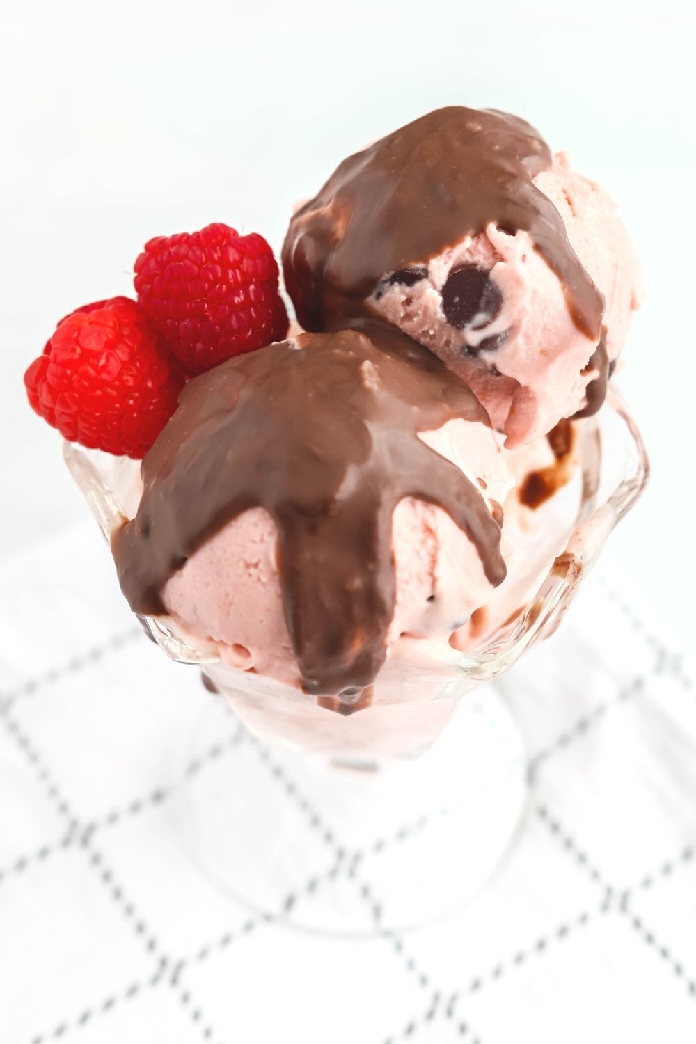 close-up side view of a glass dessert cup filled with scoops of ninja creami raspberry chocolate chip ice cream, which is garnished with raspberries and magic shell topping.