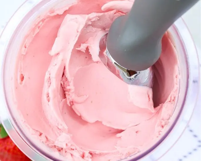 close-up view of Ninja Creami strawberry frozen yogurt with an ice cream scoop in the pint container