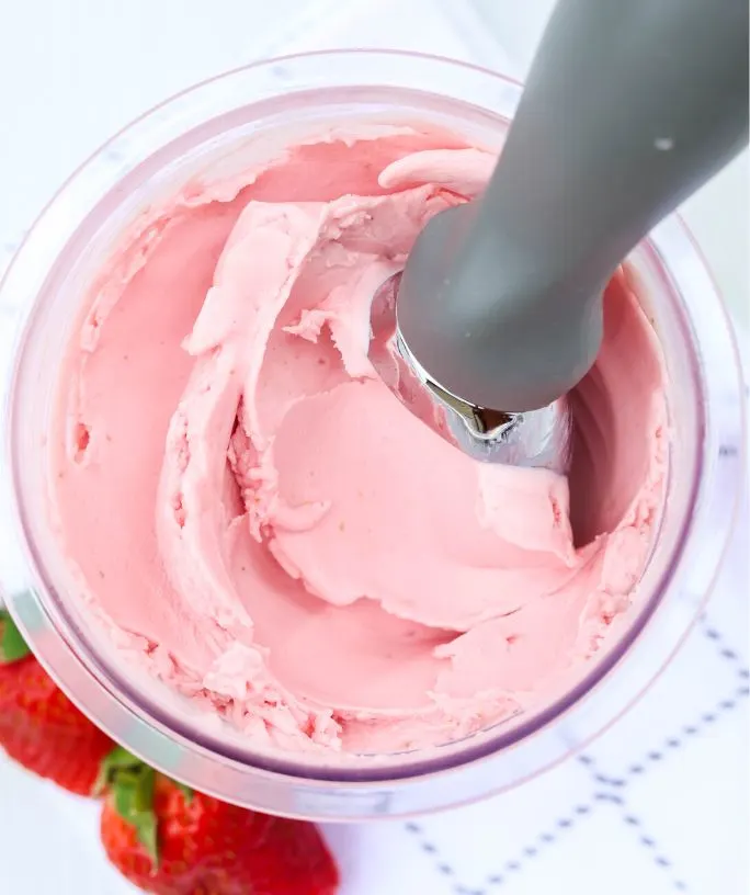 close-up view of Ninja Creami strawberry frozen yogurt with an ice cream scoop in the pint container