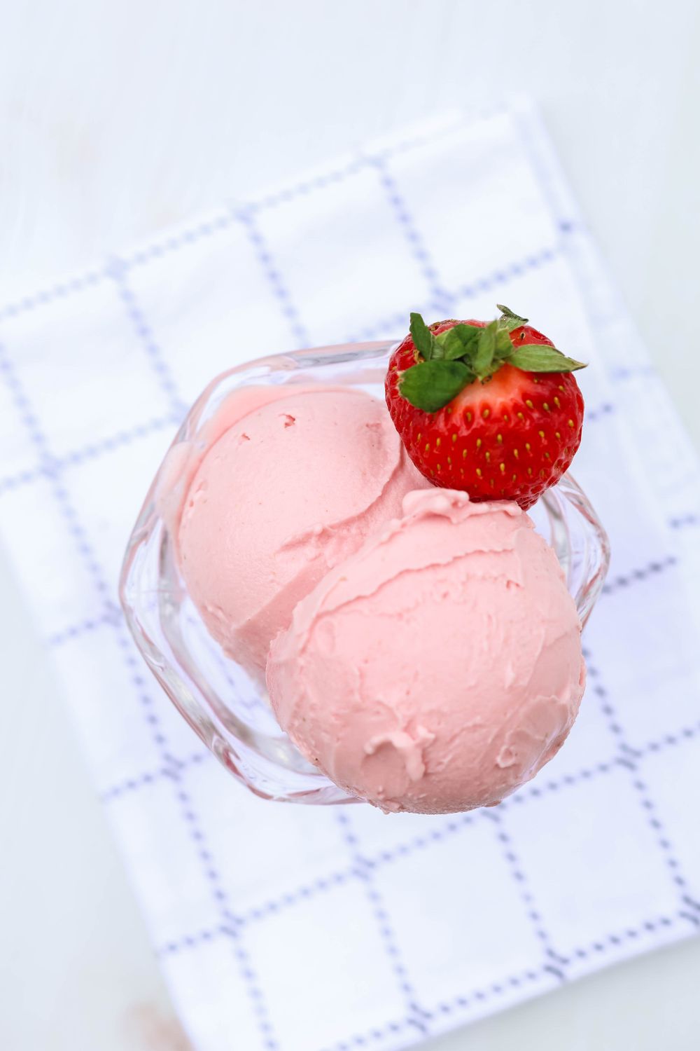 overhead view of Ninja Creami strawberry frozen yogurt in a dessert cup, garnished with a fresh strawberry
