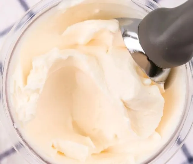 pint container of ninja creami frosted lemonade ice cream with an ice cream scoop in it.