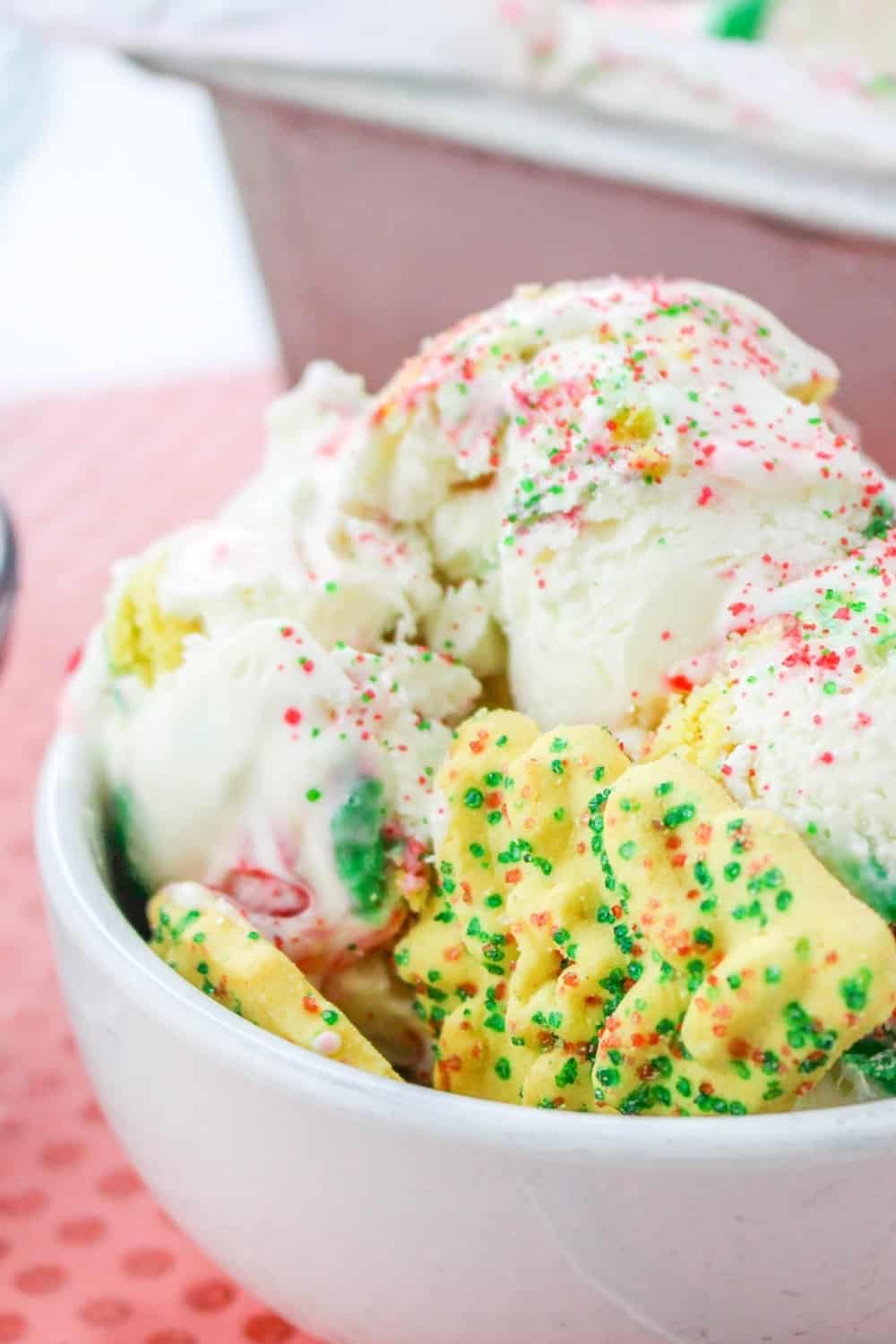 close-up view of scoops of Christmas ice cream consisting of vanilla ice cream with Christmas cookies and red and green sprinkles in it, served in a white bowl.