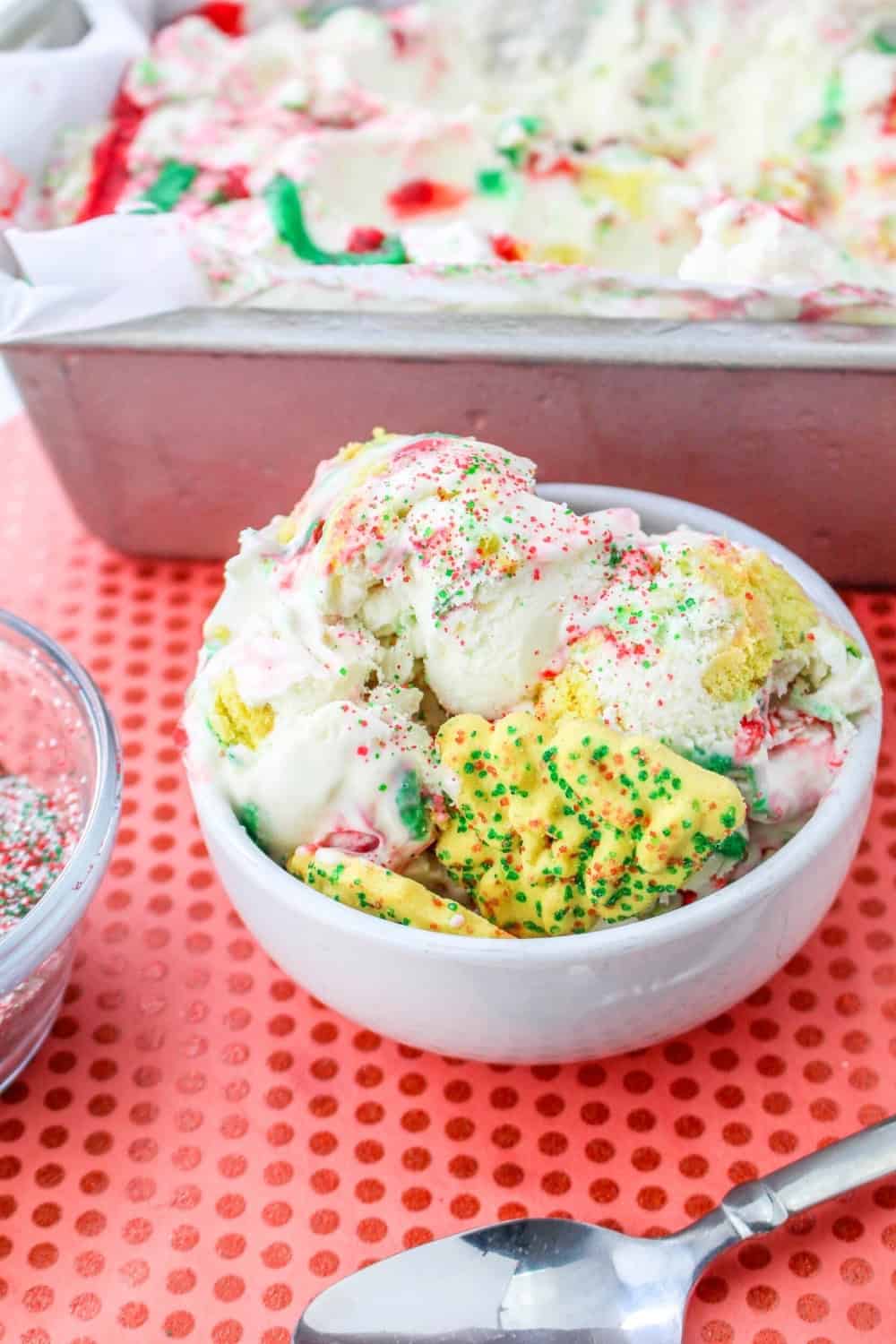 a white bowl filled with homemade Christmas cookie ice cream is in front of a loaf pan of the remaining ice cream.