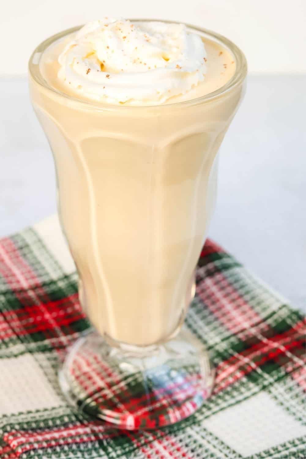 close-up side view of a glass of Ninja Slushi eggnog milkshake topped with whipped cream.