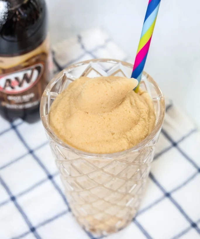 Ninja Slushi root beer float slush served in a glass with a straw. A bottle of root beer soda is in the background.