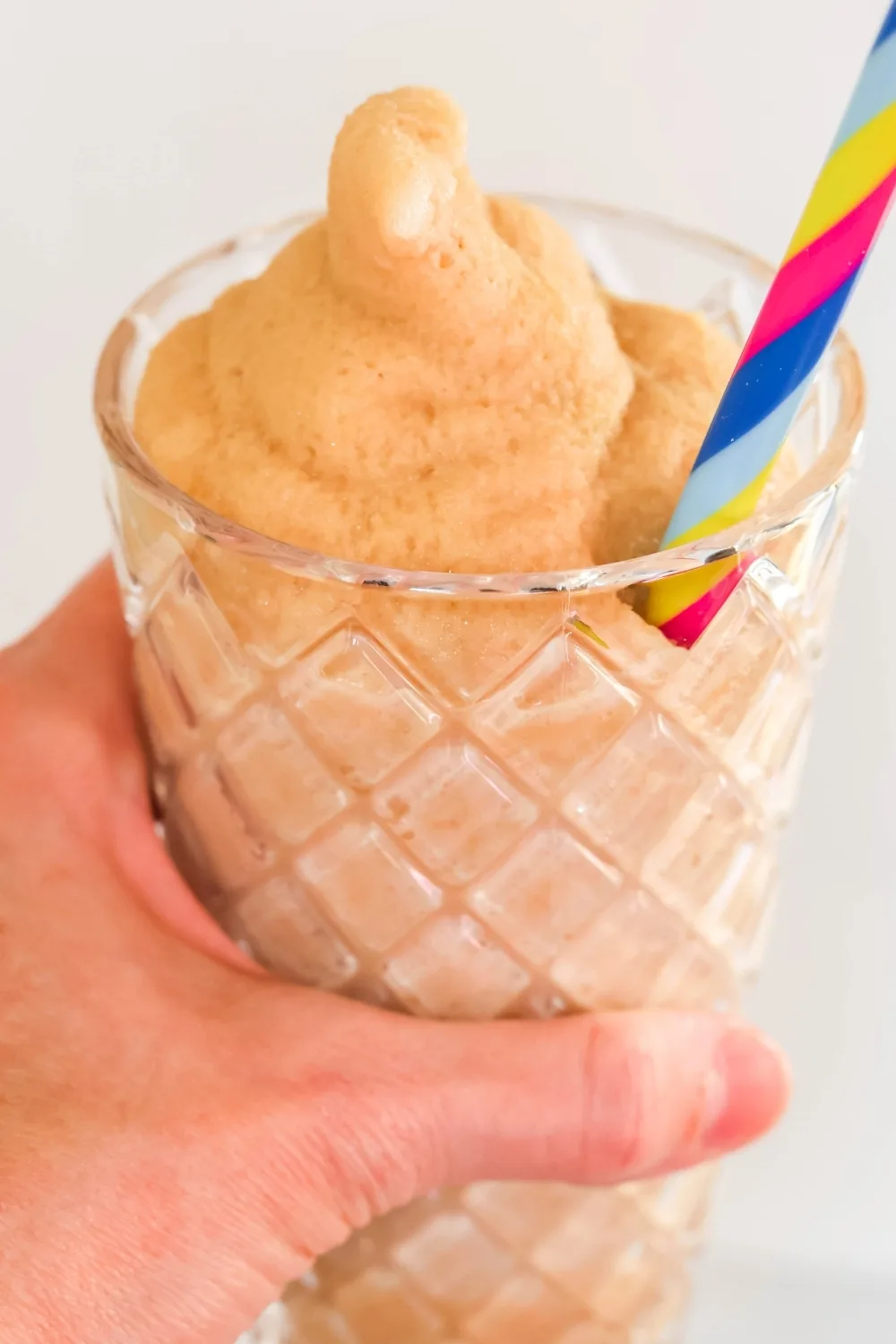 a woman's hand holds a glass of root beer cream soda slushy that was made in the Ninja Slushi.
