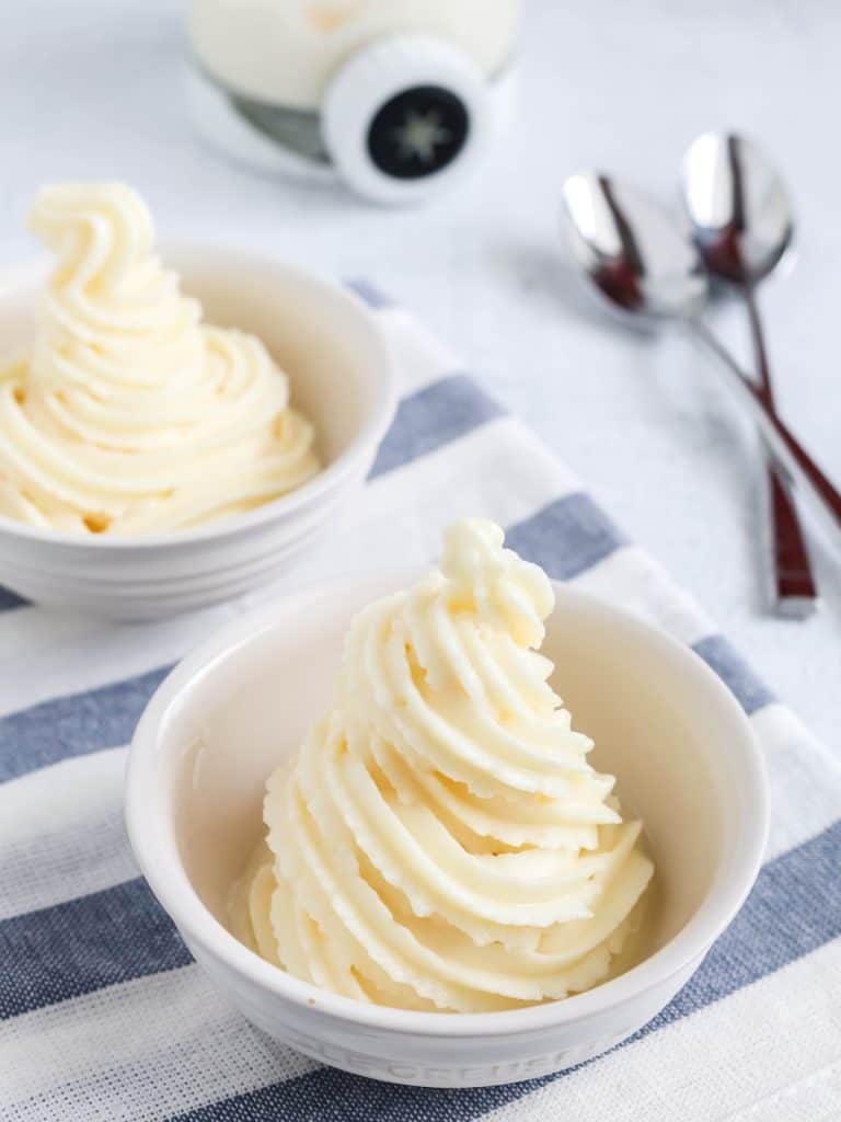 Ninja Creami Swirl Dole Whip copycat soft serve in two white bowls, with spoons and a pint container off to the side.