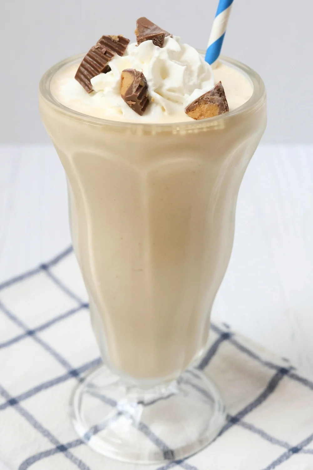 side view of a milkshake glass filled with peanut butter milkshake, which is topped with Reddi-Wip and Reese's peanut butter cups.