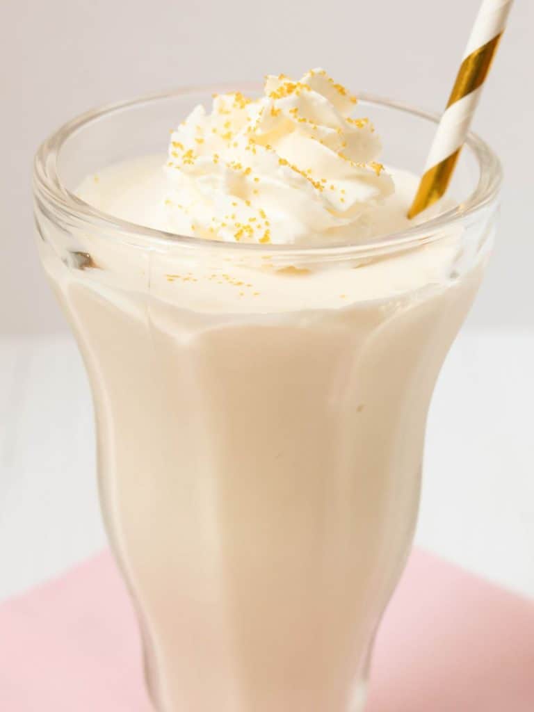 side view of a Ninja Creami vanilla milkshake served in a malt glass, garnished with whipped cream and sprinkles, served with a striped straw.