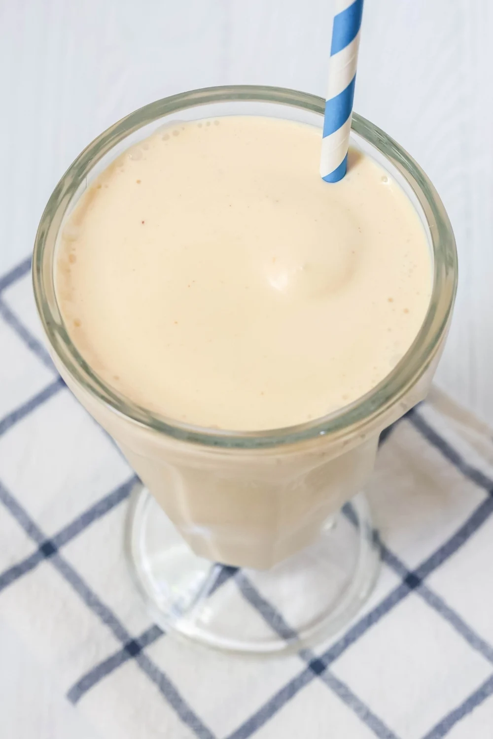 Ninja Creami milkshake made with peanut butter, served in a glass without toppings. A blue and white striped straw is in the shake.