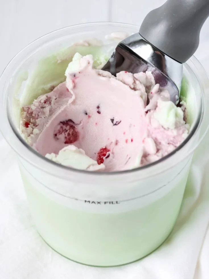 Ninja Creami pistachio cherry ice cream in a pint container with an ice cream scoop.