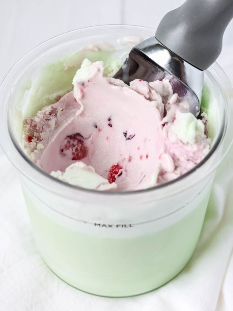Ninja Creami pistachio cherry ice cream in a pint container with an ice cream scoop.