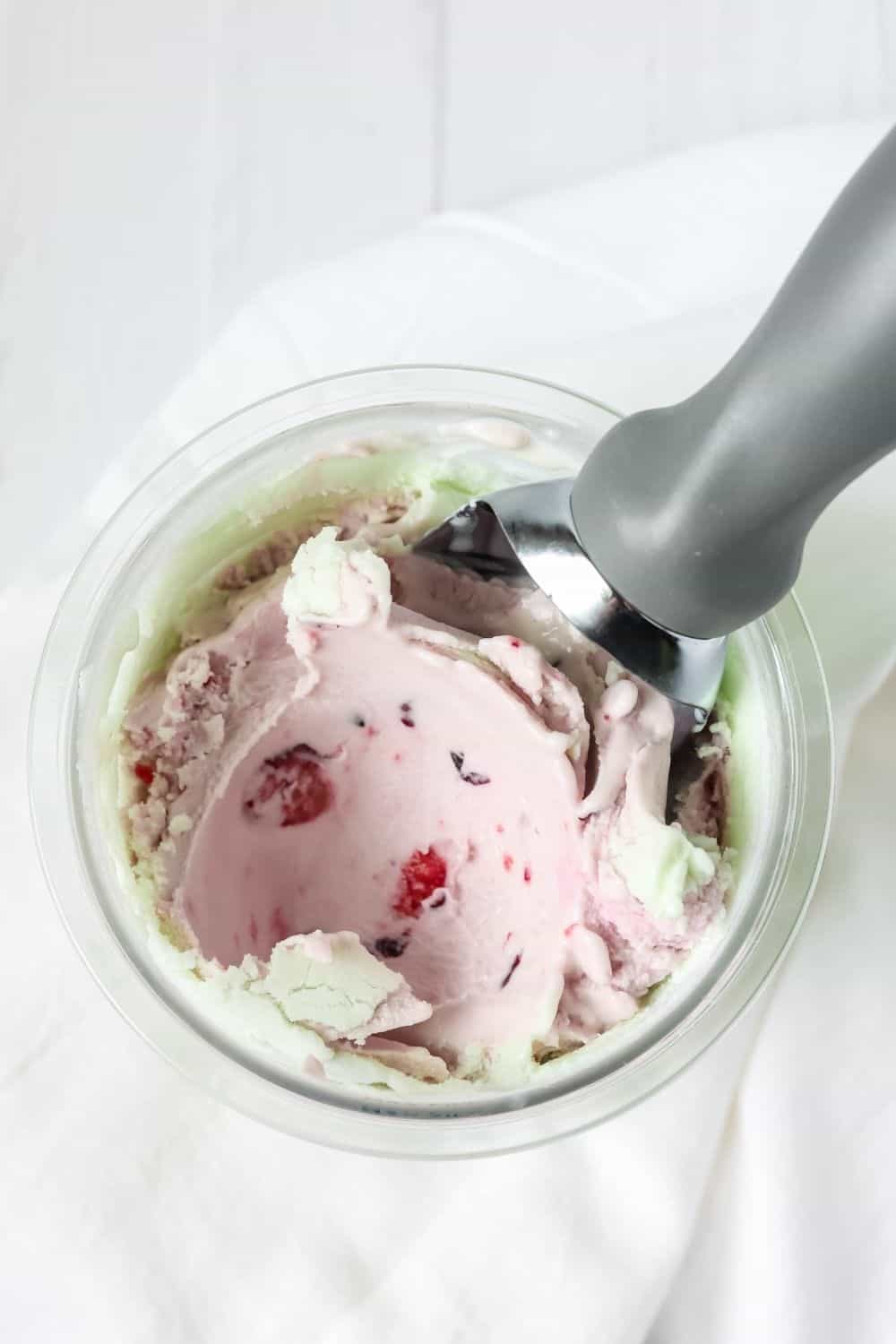 overhead view of a pint container of pistachio ice cream with fresh cherries mixed in.