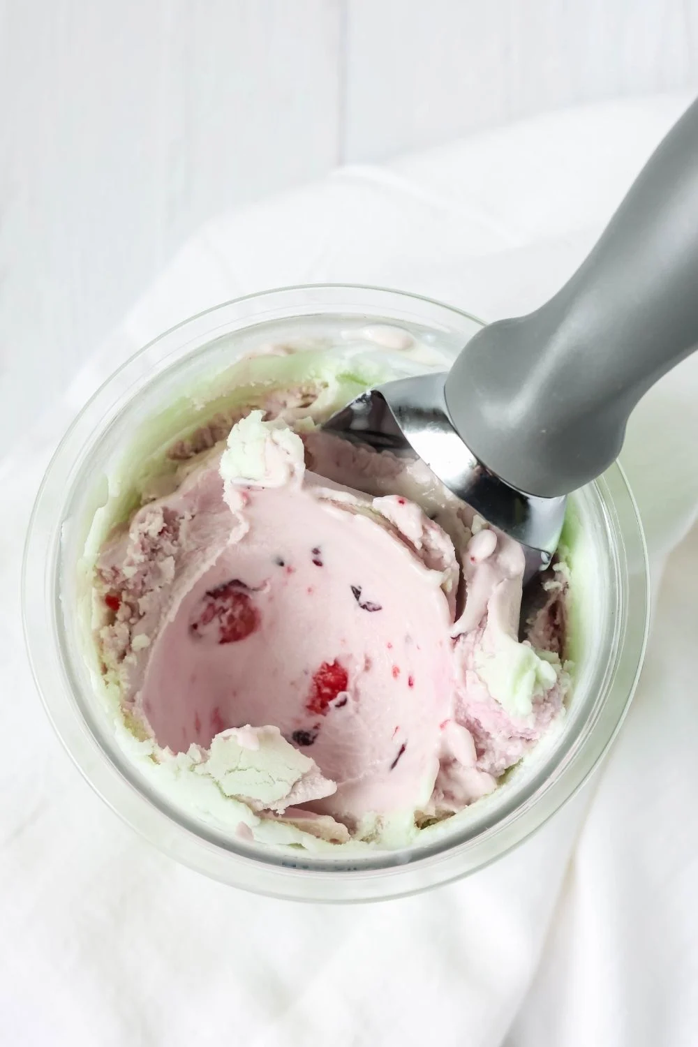 overhead view of a pint container of pistachio ice cream with fresh cherries mixed in.
