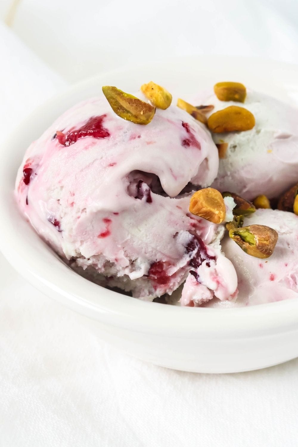 close-up side view of scoops of homemade pistachio cherry ice cream served in a white bowl.