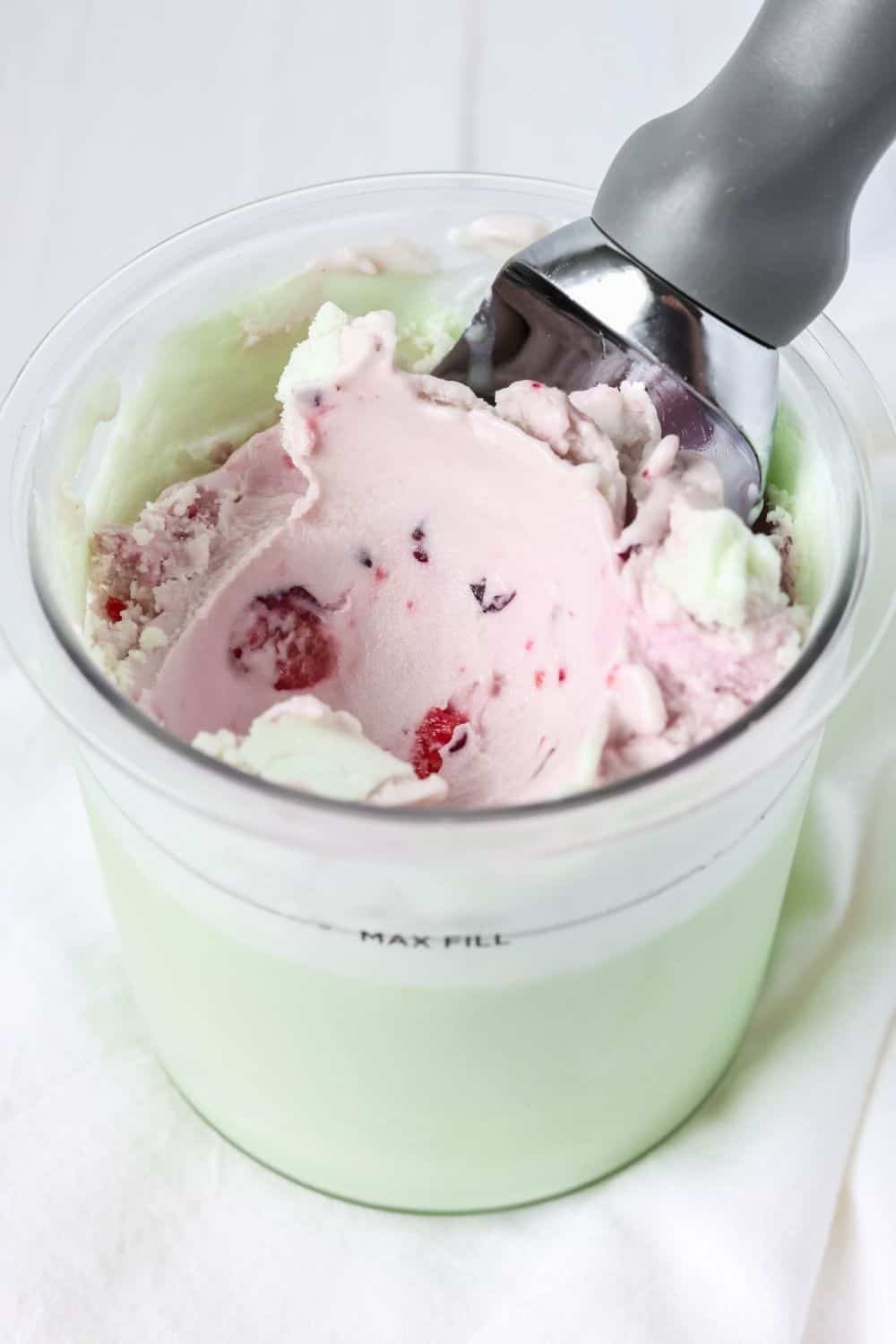 Ninja Creami pint of pistachio and cherry ice cream with an ice cream scoop in it.