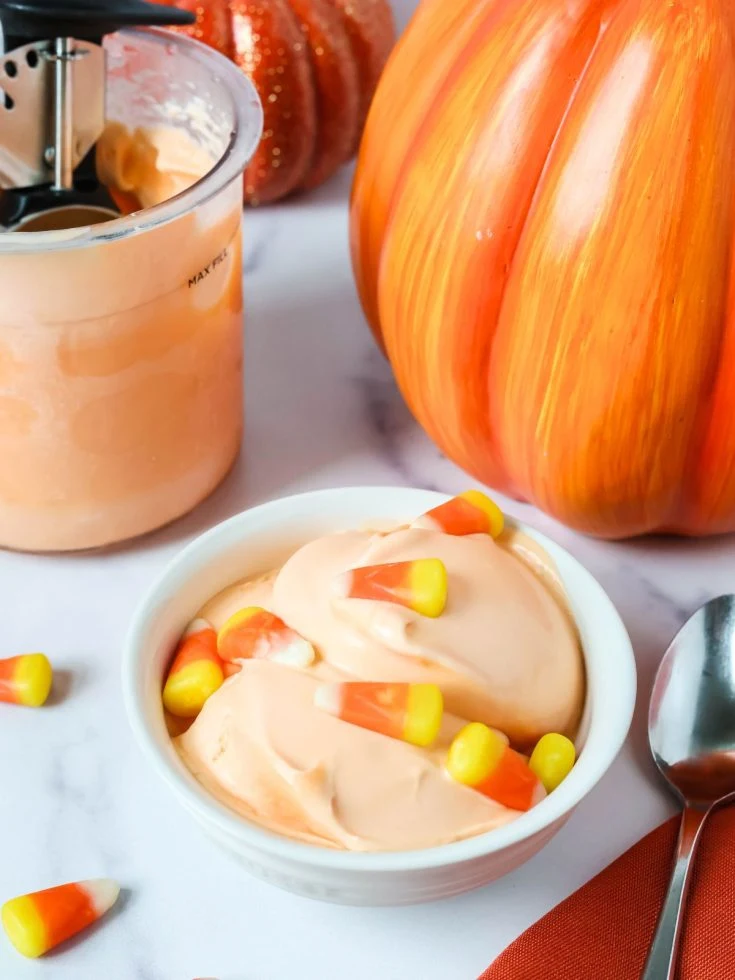 a bowl serving candy corn ice cream made in the Ninja Creami, with a pint of ice cream in the background, along with fall-themed decorations.